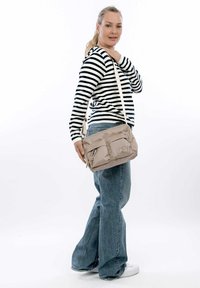 Borsa a spalla beige con due tasche frontali, in materiale tessile, tracolla regolabile e dettagli con zip, mostrata su uno sfondo neutro.