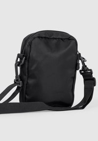 Zwarte stoffen crossbodytas met een rechthoekige vorm, ritssluiting, verstelbare riem en veilige clips. Kenmerkt zich door een gladde textuur zonder zichtbare patronen.