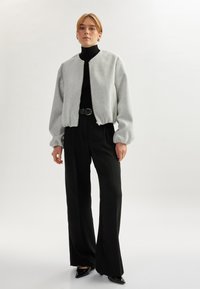 Vaaleanharmaa bomber-takki, jossa on pyöreä kaulus, vetoketjclosure ja puffi-hihat, yhdistettynä mustiin korkea vyötäröisiin housuihin ja teräväkärkisiin kenkiin.