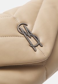 Beżowa pikowana skórzana torebka z emblematem złączonych srebrnych liter "SM" oraz widocznymi przeszyciami.