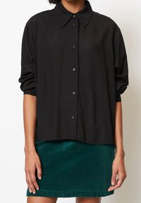 Schwarze Button-Up-Hemd mit Kragen, im entspannten Schnitt und mit hochgerollten Ärmeln, kombiniert mit einem grünen Cordrock.