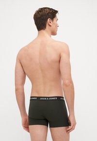 Dunkelgrüne Boxershorts mit einem breiten schwarzen Bund, der weißen Logotext zeigt, von hinten an einem Modell ohne Shirt präsentiert.