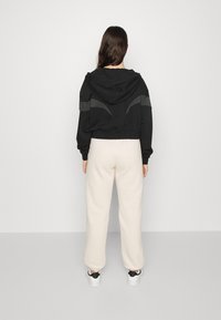 Black cropped hoodie with a hood and gray accents paired with cream-colored sweatpants, worn with white sneakers featuring black details.