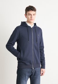 Marineblauwe zip-up hoodie van een katoenmix, met een voorkant rits, trekkoordcapuchon en zijzakken. Soepele textuur met subtiele logodetails.