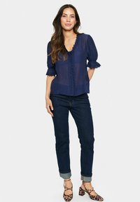 Blusa blu navy a maniche corte con scollo scallop e chiusura a bottoni. Tessuto texture, abbinata a jeans in denim scuro e scarpe con stampa leopardata.