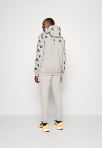 Hoodie gris con estampado de logo negro en los hombros y las mangas, combinado con joggers gris claro a juego y zapatillas naranjas y negras.