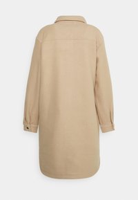 Krémová košile s límečkem, dlouhými rukávy a knoflíkovými manžetami. Měkká textura a rovný střih, s minimálními detaily šití.