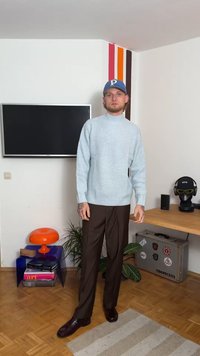 Ανοιχτό μπλε υφασμάτινο πουλόβερ με ψηλό λαιμό, συνδυασμένο με καφέ παντελόνι και σκούρα παπούτσια. Ο χώρος διαθέτει πολύχρωμο διακόσμηση και φυτά.