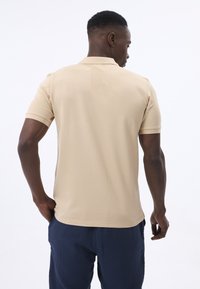 Beige Poloshirt mit kurzen Ärmeln, mit einer glatten Textur und klassischem Design, kombiniert mit marineblauen Hosen.