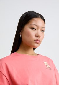 Roze katoenen t-shirt met een bloemenlogo in zacht geel en groen, met een relaxte snit en ronde halslijn. Het textuur lijkt glad te zijn.