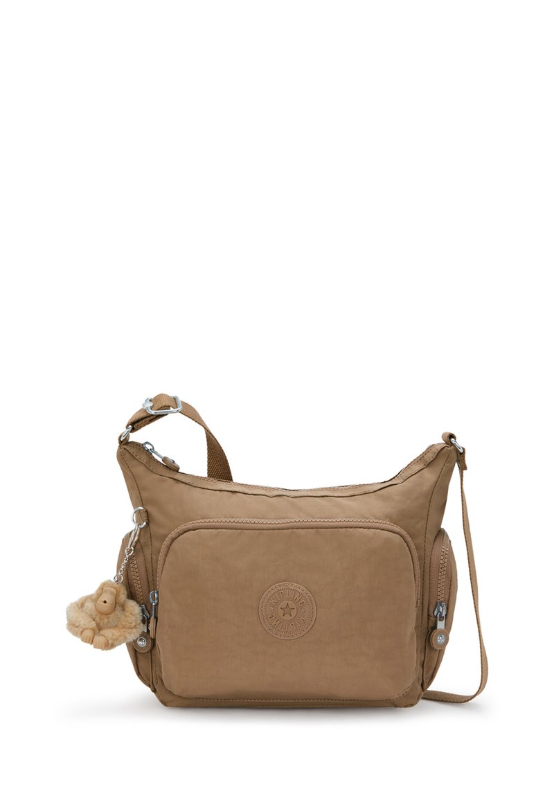 Karmelowa torebka typu crossbody wykonana z miękkiego materiału. Posiada okrągłą naszywkę z logo, kieszenie na zamek oraz brelok z pluszowym zwierzątkiem.