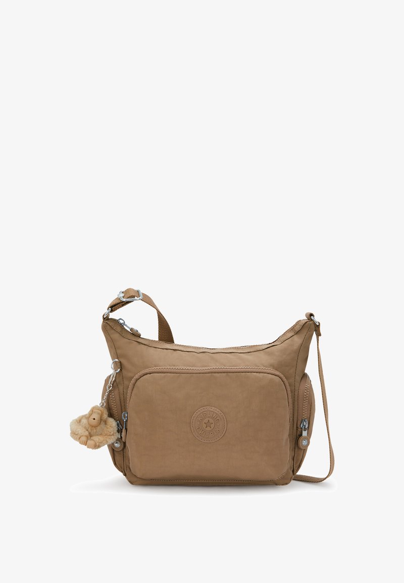 Karmelowa torebka typu crossbody wykonana z miękkiego materiału. Posiada okrągłą naszywkę z logo, kieszenie na zamek oraz brelok z pluszowym zwierzątkiem.