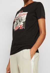 Czarny bawełniany t-shirt z grafiką z przodu przedstawiającą kwiat i słowo "LOVE" w kolorze czerwonym. Klasyczny okrągły dekolt i krótkie rękawy.