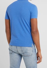 Blå kortärmad polo skjorta i mjukt material, med klassisk krage och sidoslitsar, ihop med ljus tvättade jeans.