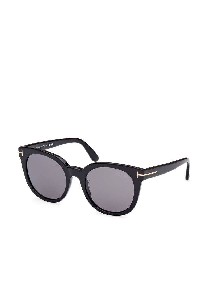 Lunettes de soleil noires surdimensionnées avec des verres foncés, monture en plastique et accents en métal doré sur les branches. Forme classique œil de chat.
