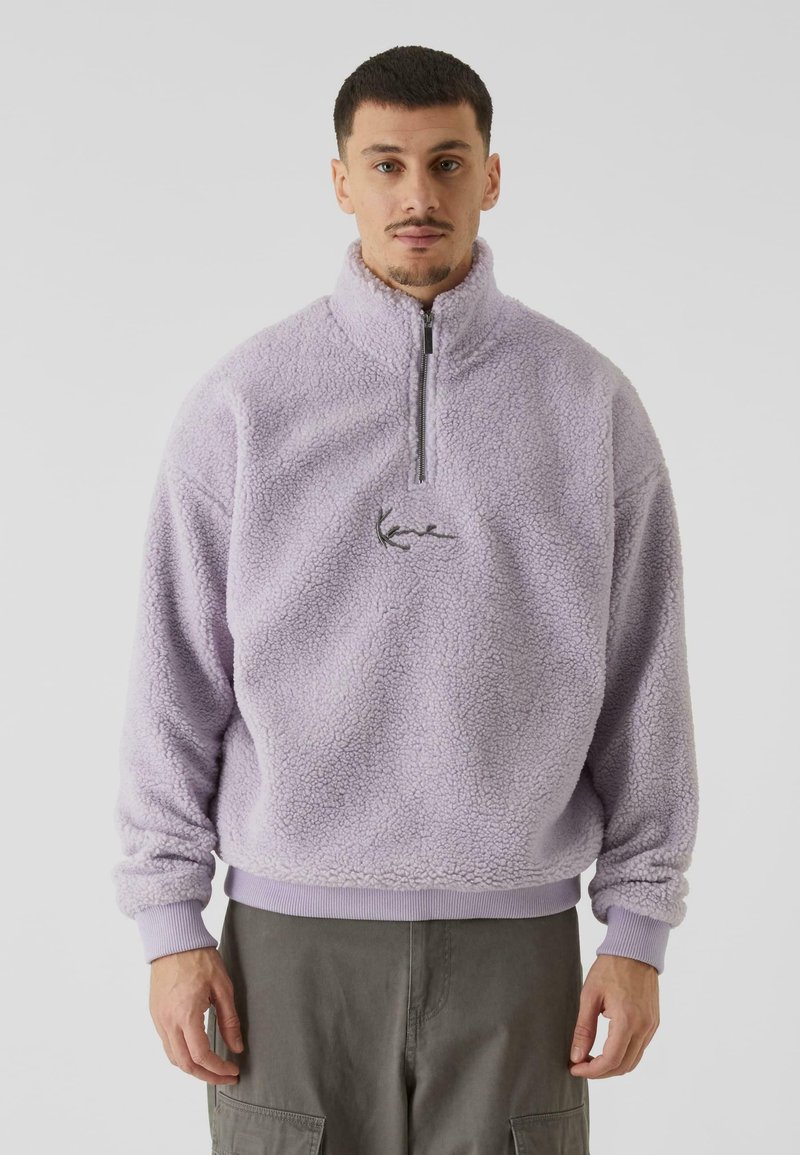 Pullover in pile viola con colletto alto e chiusura con mezza zip. Presenta un logo ricamato e polsini a coste. Materiale morbido e strutturato.