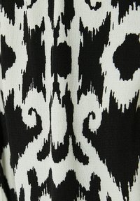 Zwart-wit gestreepte stof met een abstract ikat ontwerp met golvende lijnen en vlekken; gladde, geweven textuur.