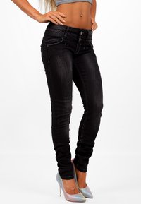 I jeans skinny neri presentano una cucitura decorativa, chiusura a due bottoni e una vestibilità slim. Indossati con tacchi alti iridescenti per creare un contrasto.