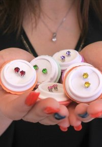 Set di orecchini a bottone esposti in eleganti custodie circolari colorate. Presenta gemme rosse, verdi, rosa, viola e gialle. Hardware in tonalità argento.
