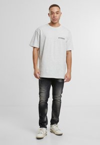 Szara bawełniana koszulka z krótkim rękawem i napisem "80s vibes" na klatce piersiowej, w połączeniu z przetartymi ciemnymi dżinsami i białymi trampkami.