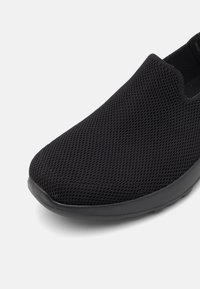 Czarne buty wsuwane z siateczkową cholewką, okrągłym czubkiem i wyściełaną podeszwą dla komfortu. Projekt jest minimalistyczny, bez widocznych elementów metalowych.