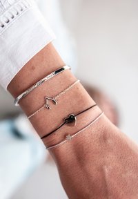 Keturi apyrankės ant riešo: sidabrinė apyrankė su įrašais, grandinėlė su sidabriniu laimės kauliuku, juodas širdies pakabukas ir sidabrinis žvaigždės pakabukas ant plonos grandinėlės.
