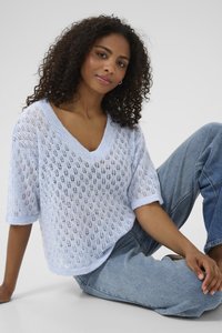 Pull en tricot bleu clair, avec un col en V et des manches courtes. Présente un motif en dentelle et une coupe décontractée, associé à un jean en denim clair.