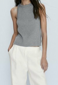 Débardeur gris côtelé à col montant, associé à un pantalon blanc ample avec poches avant et fermeture éclair.