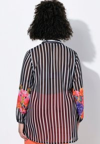 Camicia a maniche lunghe a righe bianche e nere trasparenti con accenti floreali in arancione, rosa e viola sulle maniche; taglio dritto e colletto.