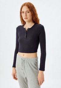 Marineblå, ribbet langærmet crop top med rund halsudskæring og tre knapstolper, parret med lysegrå ribbet bukser med snøre.