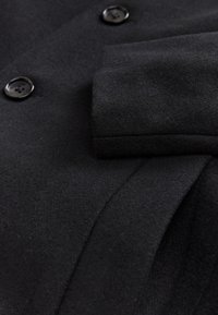 Tissu de manteau en laine noire avec deux boutons noirs et détail de poignet plié.