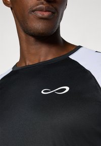 T-shirt de sport noir en tissu texturé, avec des accents blancs aux épaules et un logo infini blanc sur le devant.