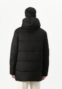 Doudoune noire, design matelassé, avec capuche et finition texturée, d'une longueur plus longue, vue de dos.