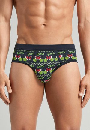 Manlig torso som bär marinblå kalsonger mönstrade med upprepade gröna Grinch-ansikten som bär röda tomteluvor och ordet "GRINCH" i grön text.