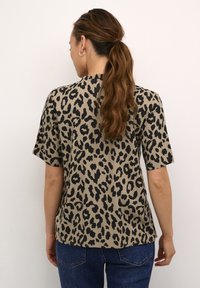 Blusa animalier in beige e nero, maniche corte, vestibilità rilassata, tessuto morbido, orlo curvo, abbinata a jeans blu scuro.