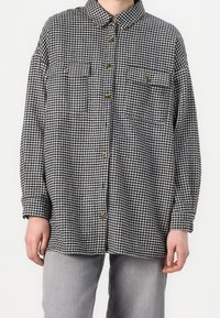 Czarna i biała koszula w wzór houndstooth z kołnierzykiem, dwiema kieszeniami na piersi i zapięciem na guziki, wykonana z teksturowanej tkaniny.