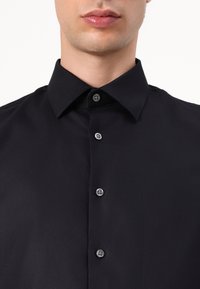 Black button-up shirt with a crisp collar, featuring gray buttons and smooth, slightly textured fabric. Close-up view from the chest up.