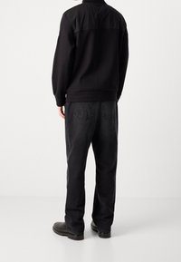 Svart sweatshirt med en slät, enfärgad överdel och en texturerad underdel, matchad med mörkgrå jeans och svarta skor.