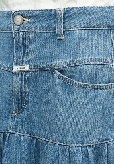 Φούστα από ανοιχτό μπλε τζιν με τελείωμα σε στρώσεις με βολάν, διαθέτει κλείσιμο με κουμπιά, μία μπροστινή τσέπη και λεπτομέρειες σε αντίθετο χρώμα ραφής.