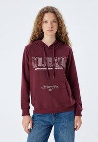 Burgundowa bluza z kapturem z przednią kieszenią, z napisem "COLORADO" w białym kolorze oraz dekoracyjnym tekstem na kieszeni w kontrastującej bieli.