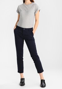 Grå kortärmad t-shirt kombinerad med marinblå byxor och svarta ankelskor. Byxorna har en slim fit och detalj med uppvikta fållar.