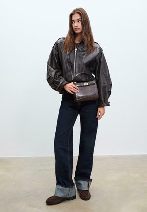 Giacca in pelle marrone con maniche oversize, abbinata a jeans in denim scuri e stivali in suede marrone. Una borsa piccola con motivo aggiunge un tocco di dettaglio.