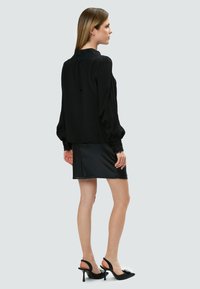 Blusa nera con maniche a palloncino e colletto in pizzo, abbinata a una gonna mini nera aderente e tacchi neri a punta con decorazioni.