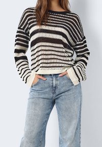 Schwarz-weiß gestreifter Pullover mit lockerem Schnitt, weitem Ausschnitt und gerippten Bündchen, kombiniert mit hellblauen Jeans.