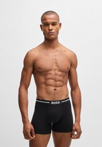 Black boxer briefs featuring a contrasting elastic waistband with “BOSS” logo. Close-fitting design, smooth texture, and mid-thigh length.