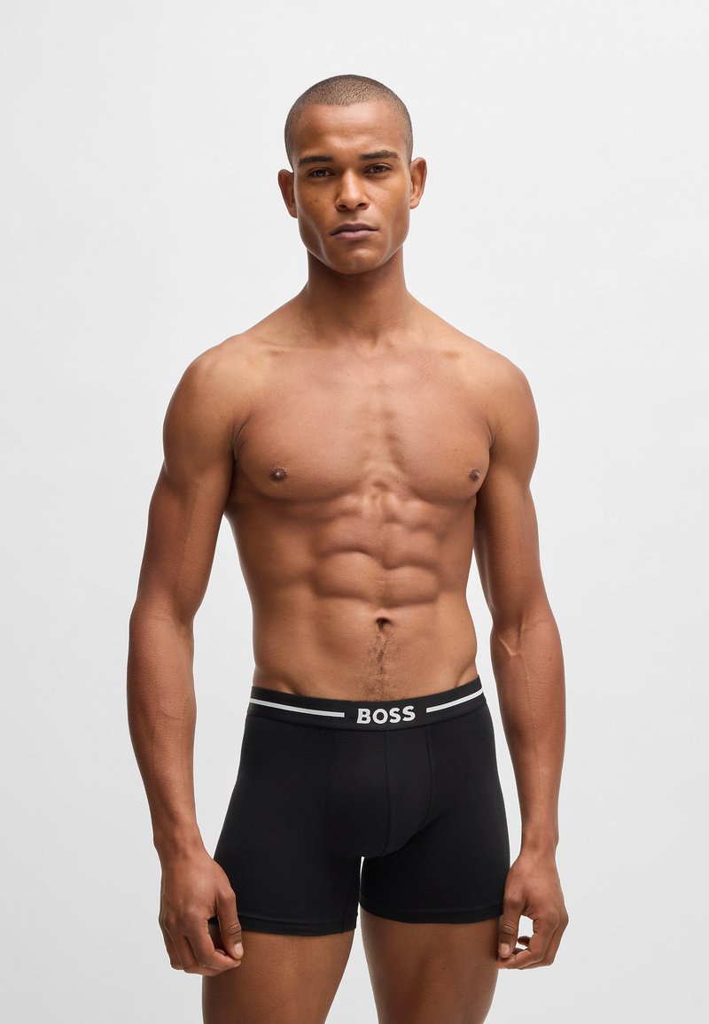 Black boxer briefs featuring a contrasting elastic waistband with “BOSS” logo. Close-fitting design, smooth texture, and mid-thigh length.