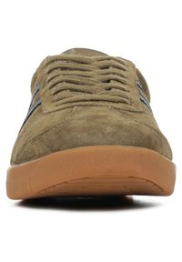 Suède sneakers in tan met zwarte accenten, voorzien van platte veters en een gestructureerde rubberen zool voor grip. Vooraanzicht benadrukt de gehaakte details op de tong.