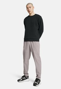 Zwarte sweatshirt met een ronde hals, gecombineerd met lichtgrijze broeken met een relaxte pasvorm. Schoenen zijn zwart-witte sportschoenen.