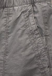 Tela gris con una cinturilla elástica y costuras verticales y diagonales detalladas en un bolsillo de la prenda.