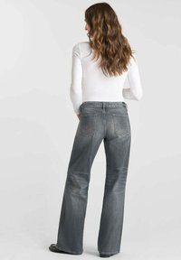 Jean gris évasés avec un délavage, poches arrière avec détails de couture, accompagnés d'un haut à manches longues blanc.